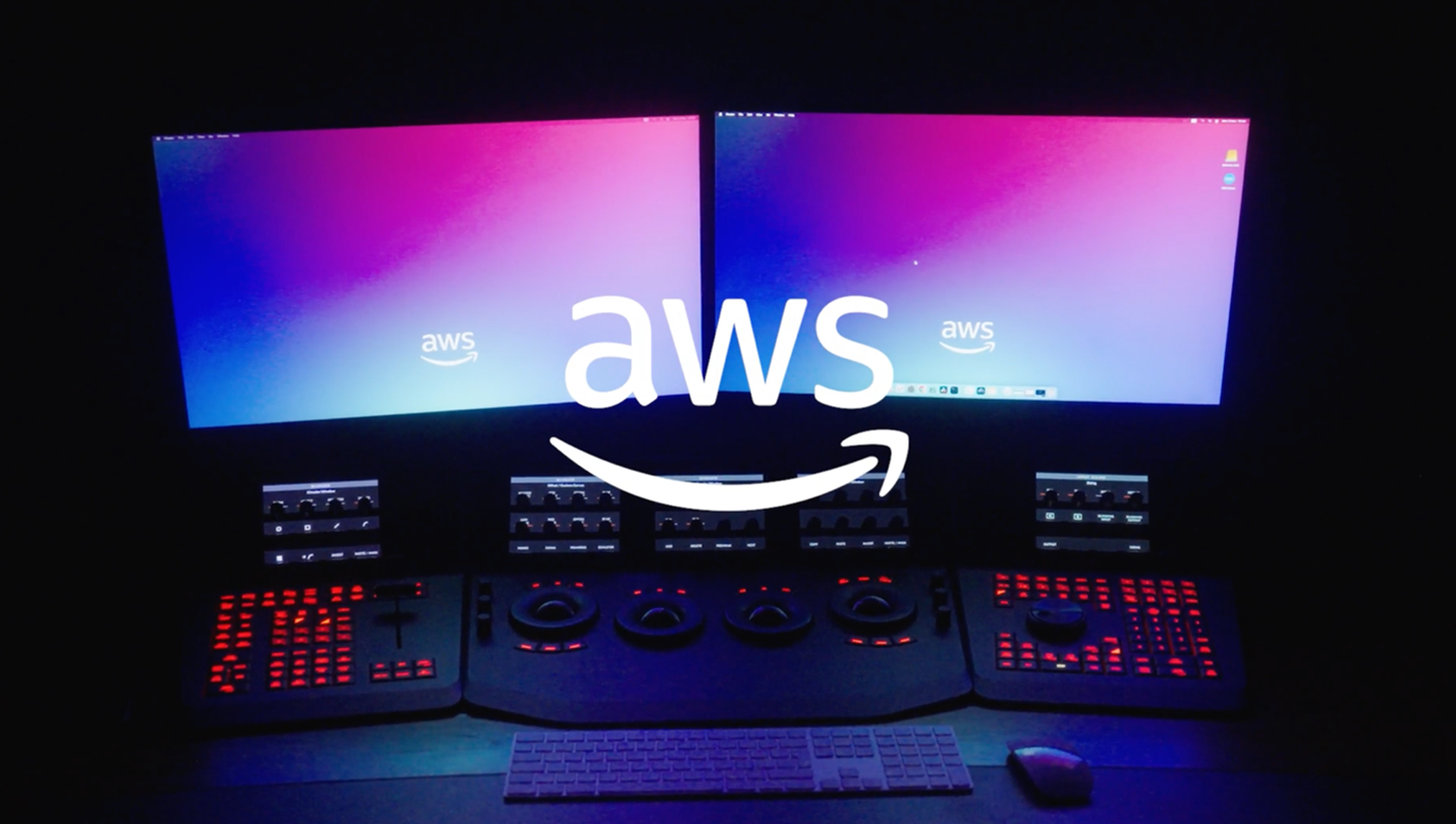 Dual-monitor workstation setup displaying the AWS logo on gradient screens, with a professional video color grading console below featuring illuminated red controls, a keyboard, and a mouse in a dimly lit room.